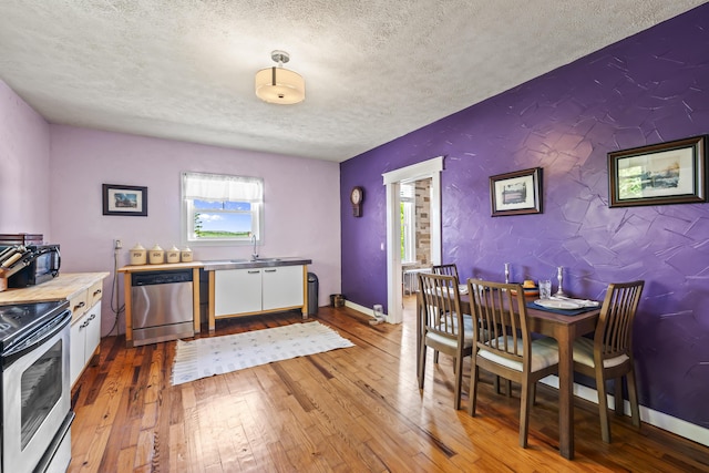 dining area with an accent wall, baseboards, light wood finished floors, and a textured ceiling