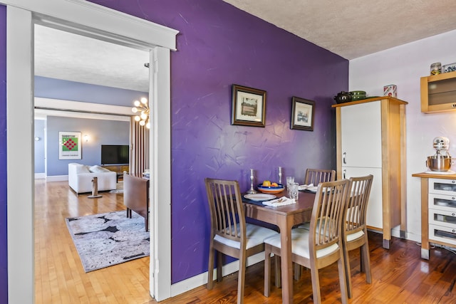 dining area featuring a textured ceiling, baseboards, wood finished floors, an inviting chandelier, and an accent wall