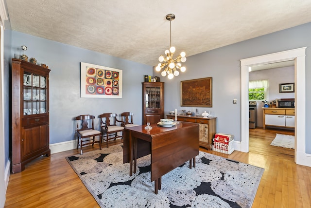 dining space featuring baseboards, light wood-type flooring, a textured ceiling, and a chandelier