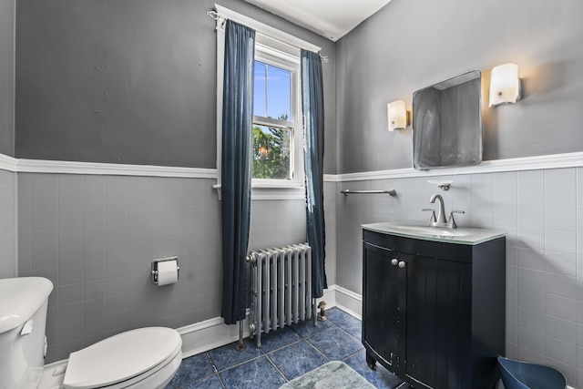 bathroom featuring a wainscoted wall, tile patterned floors, toilet, radiator heating unit, and tile walls