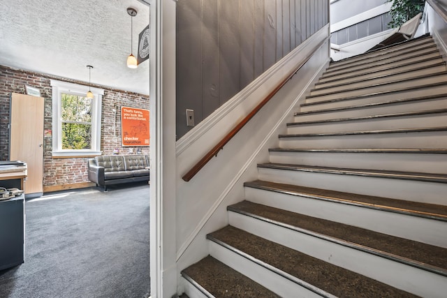 stairway with carpet flooring, brick wall, and a textured ceiling