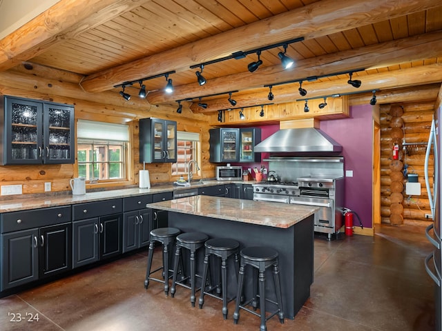 kitchen with a center island, wall chimney exhaust hood, log walls, beamed ceiling, and stainless steel appliances