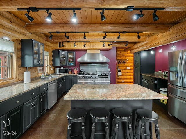 kitchen featuring beam ceiling, a center island, log walls, wall chimney range hood, and appliances with stainless steel finishes