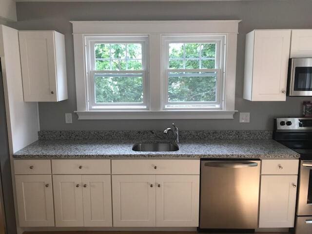 kitchen featuring a wealth of natural light, sink, stainless steel appliances, and white cabinetry