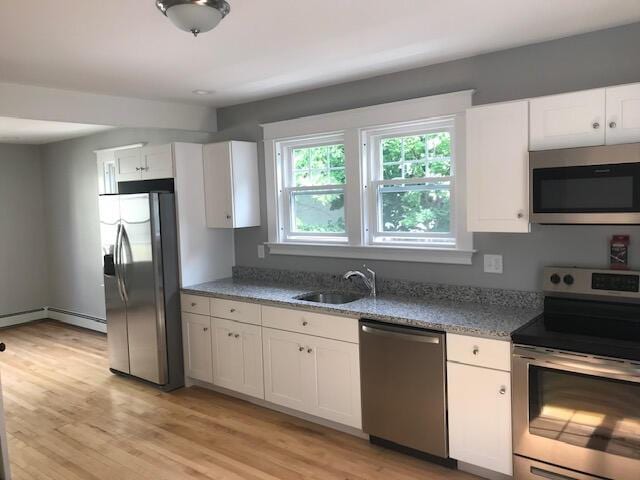 kitchen with baseboard heating, appliances with stainless steel finishes, white cabinetry, sink, and light wood-type flooring