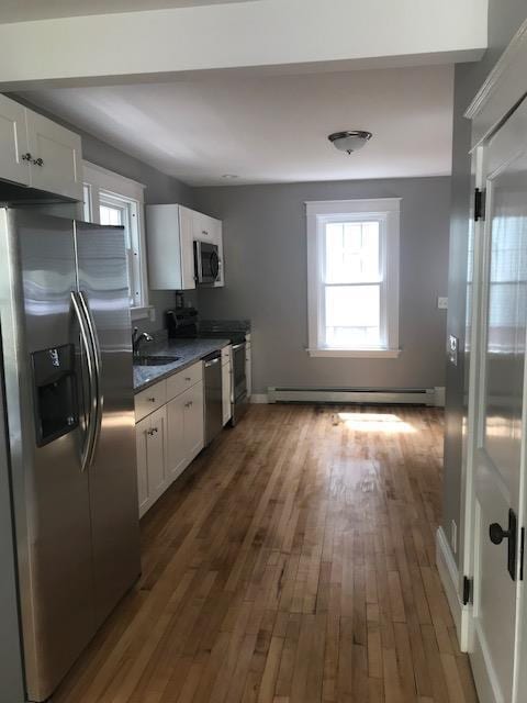 kitchen featuring white cabinetry, appliances with stainless steel finishes, dark wood-type flooring, baseboard heating, and sink