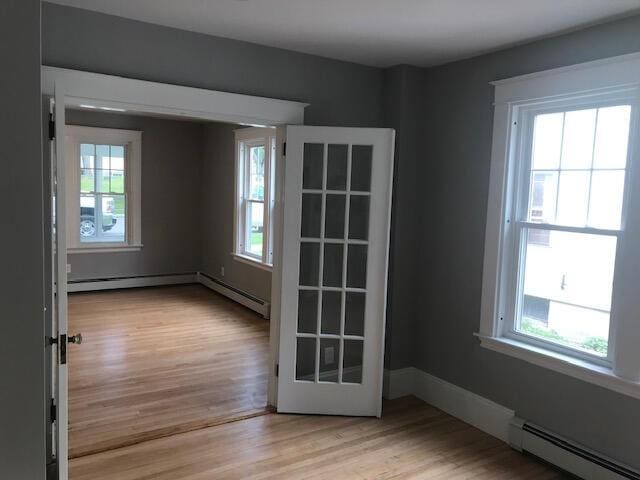 unfurnished room featuring french doors, light hardwood / wood-style flooring, and a baseboard radiator