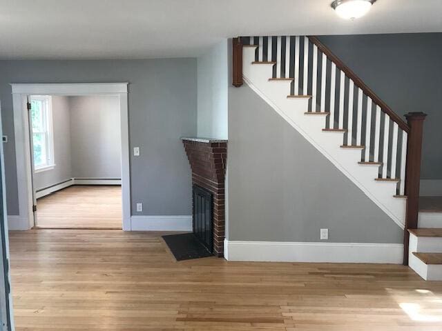 stairway featuring a brick fireplace, hardwood / wood-style floors, and a baseboard radiator