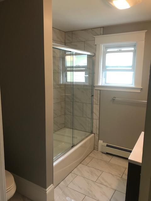 full bathroom with a baseboard radiator, combined bath / shower with glass door, vanity, and toilet