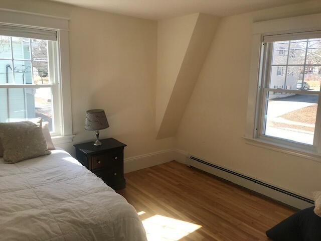 bedroom with a baseboard heating unit, wood-type flooring, and multiple windows