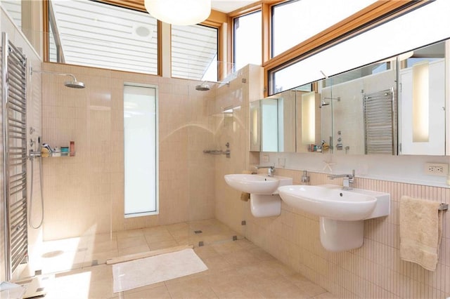 bathroom with dual sinks, tiled shower, tile walls, and tile patterned floors