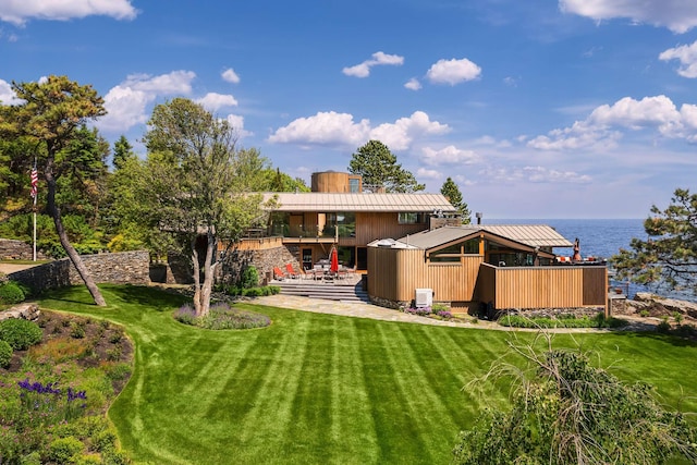 back of house with central AC unit, a patio area, a lawn, and a water view