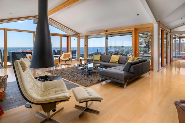 living room featuring lofted ceiling with beams, a wood stove, a wall of windows, a water view, and light hardwood / wood-style flooring