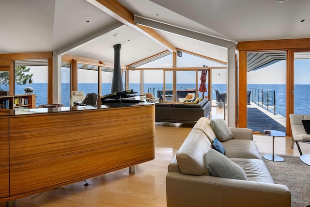 living room featuring a water view, a wood stove, vaulted ceiling with beams, and light hardwood / wood-style floors