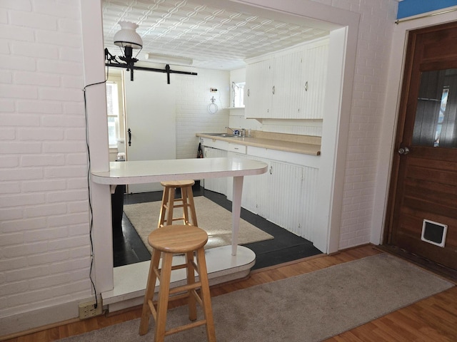 kitchen featuring light countertops, a barn door, white cabinets, brick wall, and wood finished floors