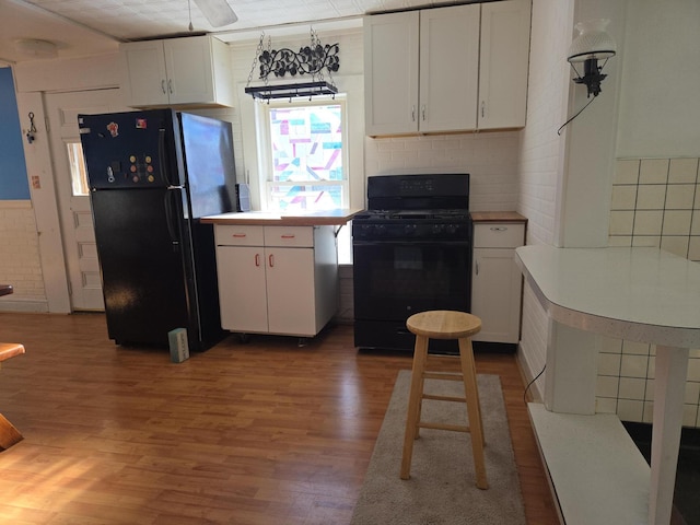 kitchen with black appliances, white cabinets, wood finished floors, and light countertops