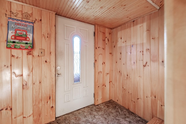 foyer with carpet floors, wooden walls, and wood ceiling