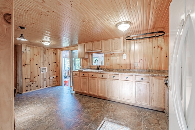 kitchen with wood walls, sink, white fridge with ice dispenser, light brown cabinetry, and decorative light fixtures