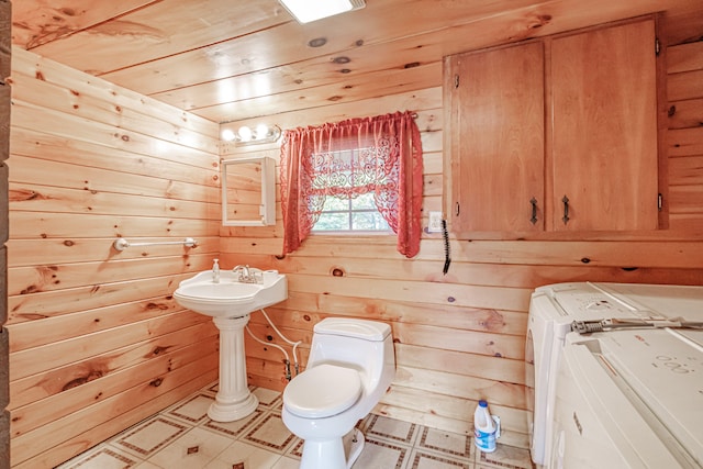 bathroom featuring washing machine and dryer, wooden walls, sink, and toilet