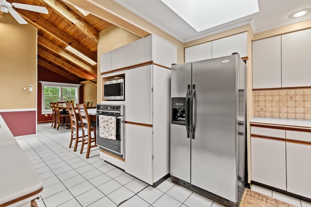 kitchen featuring lofted ceiling with skylight, light tile patterned floors, appliances with stainless steel finishes, white cabinetry, and ceiling fan