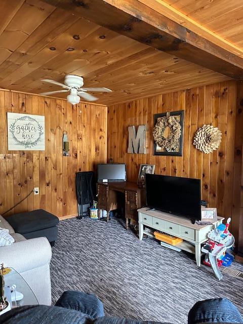 living room with ceiling fan, wood walls, wooden ceiling, and beam ceiling