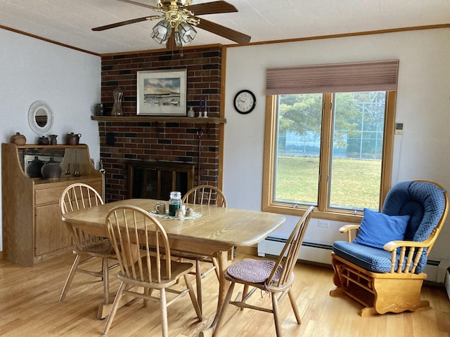 dining area with a brick fireplace, plenty of natural light, ornamental molding, and light wood-type flooring