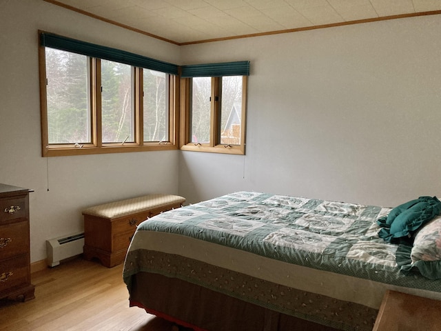 bedroom featuring a baseboard heating unit, light hardwood / wood-style flooring, and ornamental molding