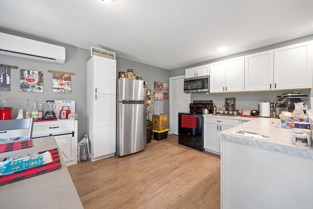 kitchen featuring appliances with stainless steel finishes, light wood-type flooring, white cabinetry, and a wall mounted AC