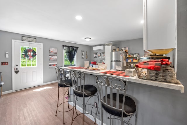 kitchen with stainless steel refrigerator, a wall unit AC, kitchen peninsula, light hardwood / wood-style floors, and a breakfast bar