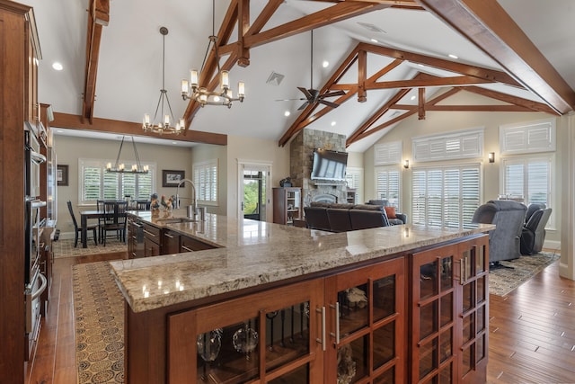 kitchen with light stone countertops, decorative light fixtures, a fireplace, a large island, and high vaulted ceiling