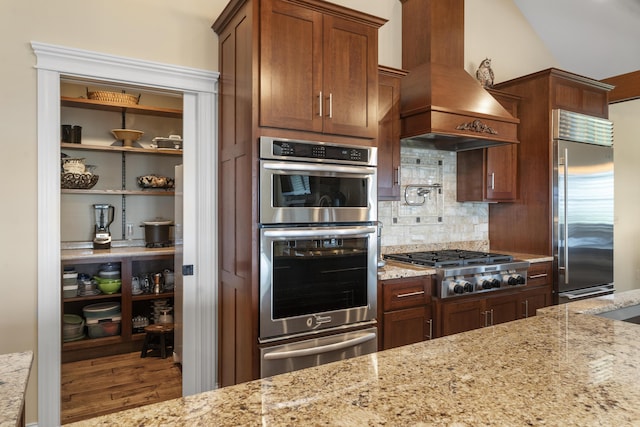 kitchen with light stone countertops, premium range hood, stainless steel appliances, and tasteful backsplash