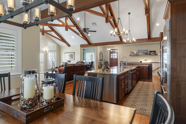 kitchen featuring dark hardwood / wood-style floors, a kitchen island with sink, pendant lighting, light stone counters, and beamed ceiling