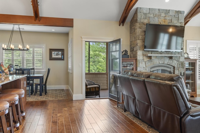 living room with a stone fireplace, a healthy amount of sunlight, dark hardwood / wood-style floors, a notable chandelier, and beamed ceiling