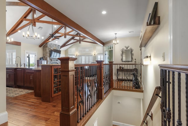 staircase with a fireplace, hardwood / wood-style floors, beam ceiling, sink, and high vaulted ceiling