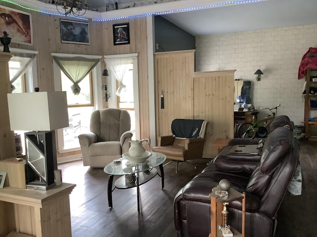 living room with wood walls, dark wood-type flooring, brick wall, and a chandelier