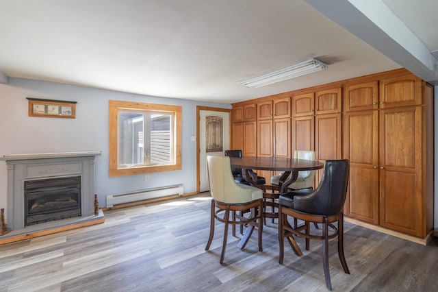 dining room with a baseboard heating unit, wood finished floors, and a glass covered fireplace