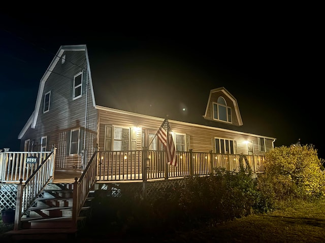 back of house at night featuring a gambrel roof and a deck