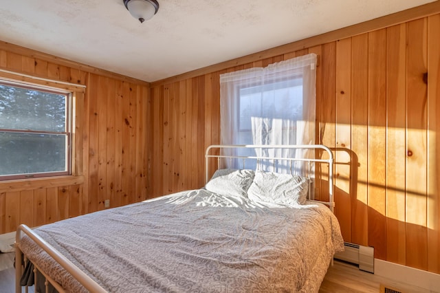 bedroom with wooden walls, multiple windows, wood finished floors, and a baseboard radiator