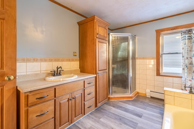 bathroom with hardwood / wood-style flooring, crown molding, baseboard heating, tile walls, and vanity