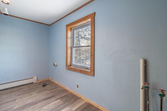 empty room with baseboard heating, crown molding, light wood-type flooring, and baseboards