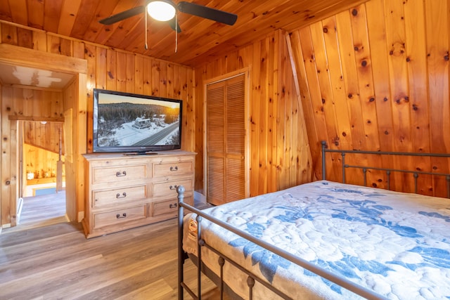 bedroom with ceiling fan, light hardwood / wood-style floors, wooden ceiling, a closet, and wood walls