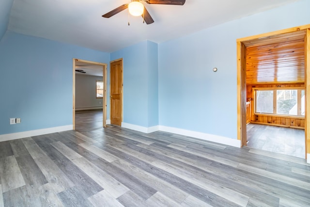 empty room with baseboard heating, hardwood / wood-style floors, a healthy amount of sunlight, and ceiling fan