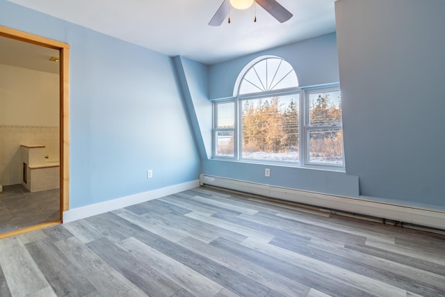 unfurnished bedroom featuring wood finished floors, baseboards, a baseboard radiator, ceiling fan, and ensuite bathroom