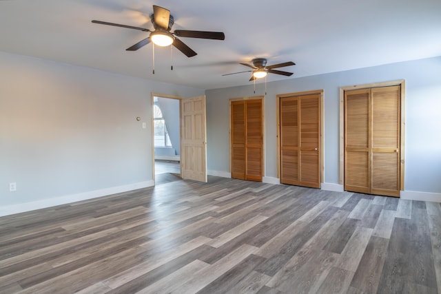 unfurnished bedroom featuring ceiling fan, baseboards, multiple closets, and wood finished floors