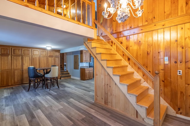 stairway featuring a towering ceiling, hardwood / wood-style floors, an inviting chandelier, and wood walls