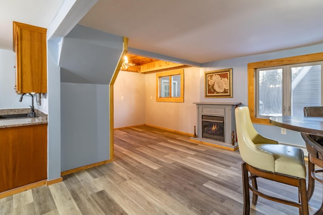 home office featuring a sink, baseboards, a warm lit fireplace, and light wood finished floors