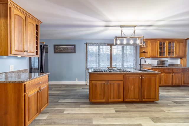 kitchen with sink, dark stone countertops, decorative light fixtures, stainless steel gas stovetop, and light wood-type flooring