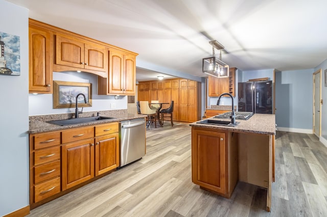 kitchen featuring light wood-type flooring, freestanding refrigerator, a sink, stainless steel dishwasher, and brown cabinets