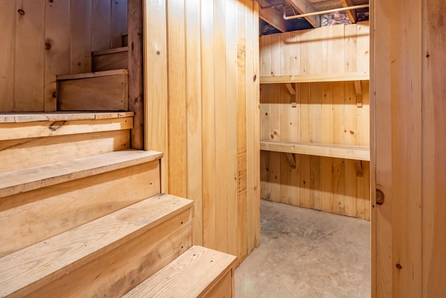 staircase featuring wooden walls and concrete flooring