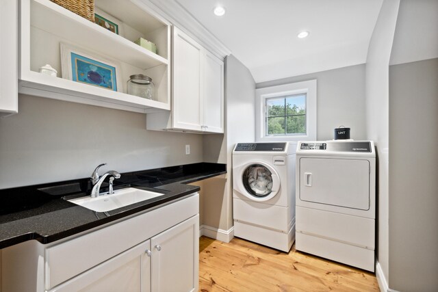 washroom featuring sink, separate washer and dryer, light hardwood / wood-style flooring, and cabinets